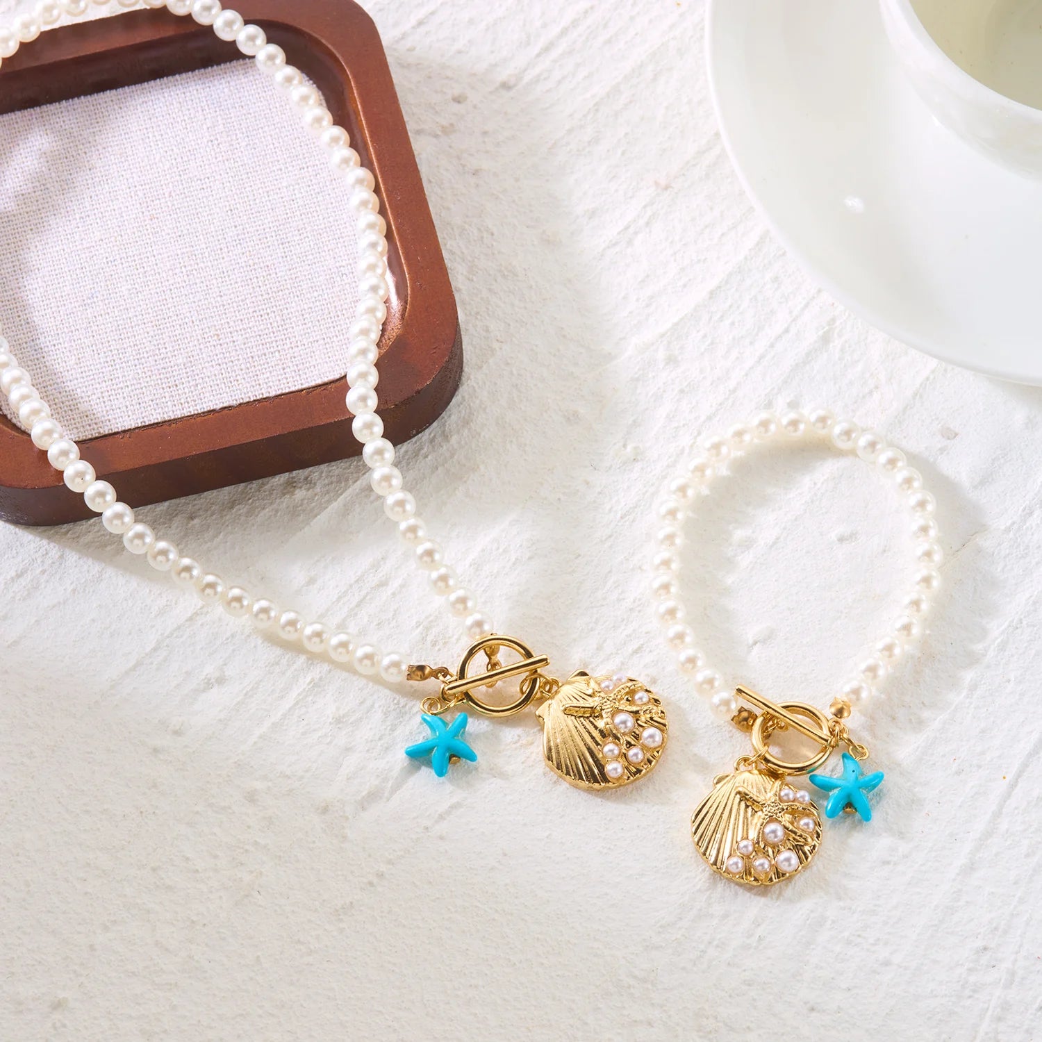 Flat lay of the Cove imitation pearl necklace and bracelet set with shell and starfish charms