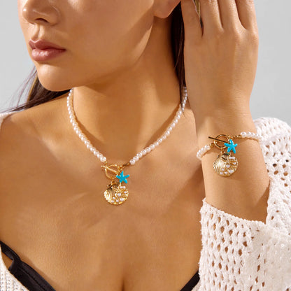 Model wearing the Cove imitation pearl necklace and bracelet with gold-tone scallop shell and turquoise starfish charms
