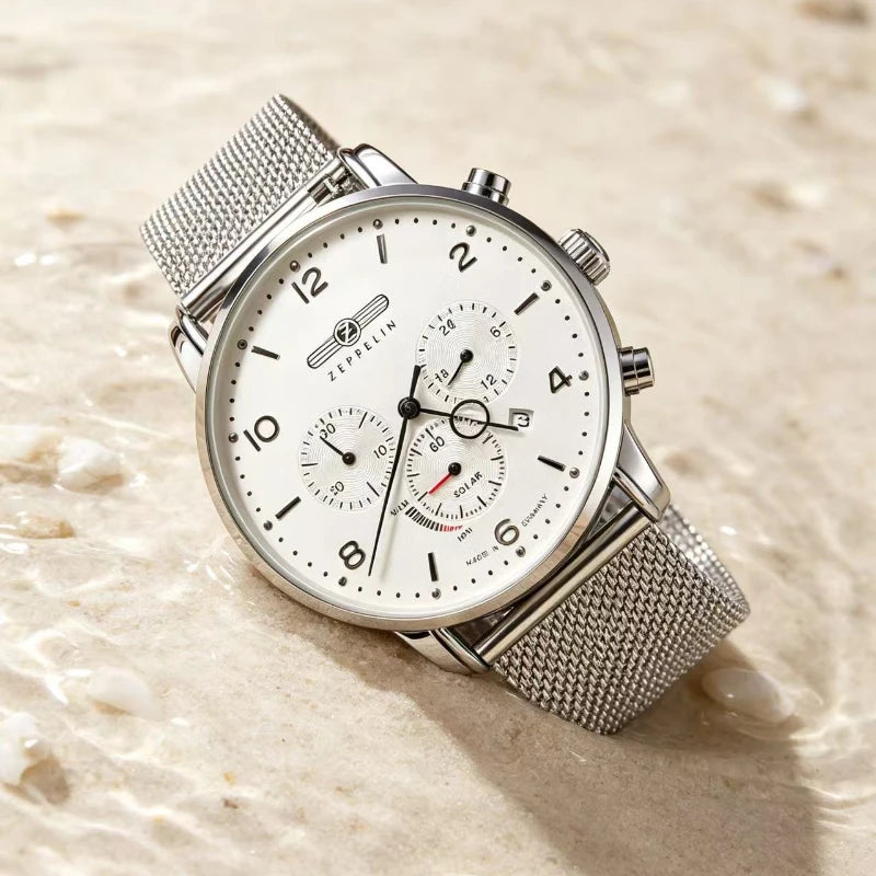 Silver mesh bracelet watch resting on wet sand