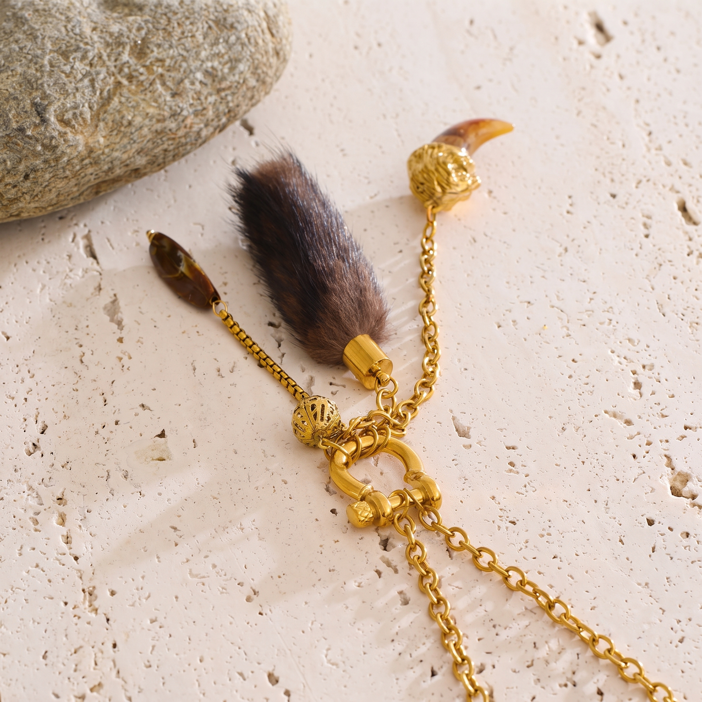 Close-up detail of Briar necklace charms: faux fur tassel, amber-tone bead, and resin claw pendant