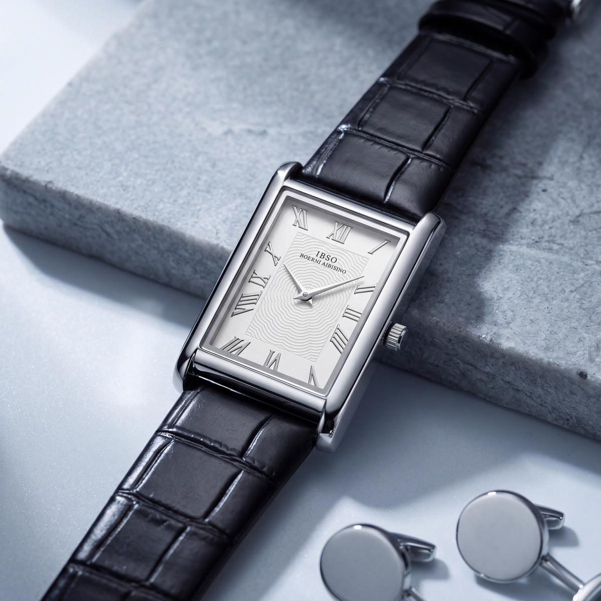 Carlyle rectangular dress watch in silver-tone, angled on a grey stone slab beside a pair of silver cufflinks