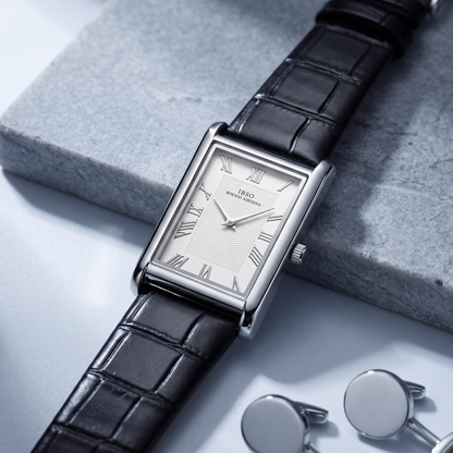 Carlyle rectangular dress watch in silver-tone, angled on a grey stone slab beside a pair of silver cufflinks