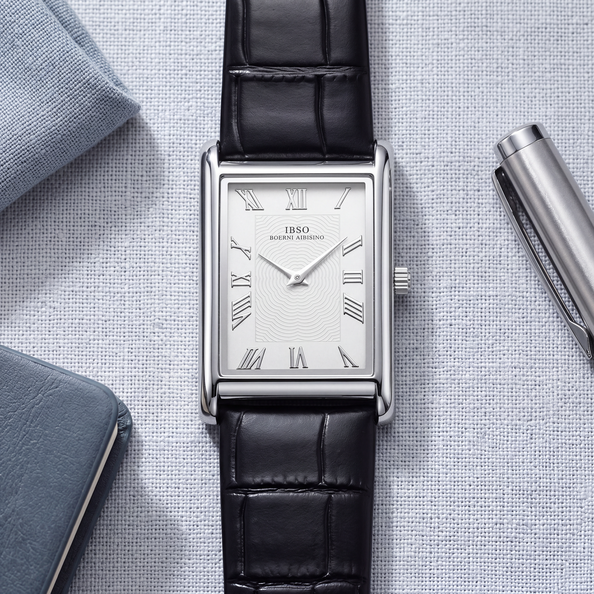 Carlyle rectangular dress watch in silver-tone laid flat on grey linen with a pen and pocket square