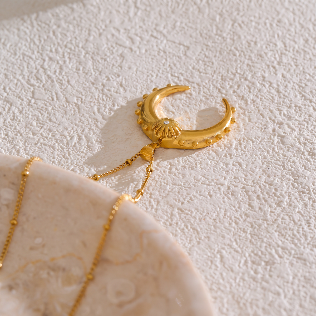Celeste Moon Pendant Necklace in gold, styled on a textured tabletop