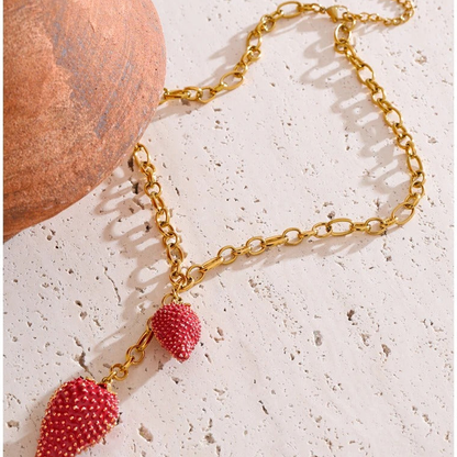 Jolie Strawberry Charm Necklace laid on stone beside a terracotta vessel