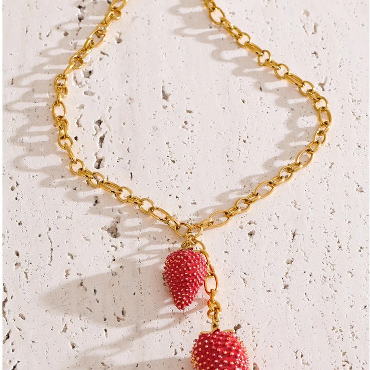 Jolie Strawberry Charm Necklace flat lay on textured stone