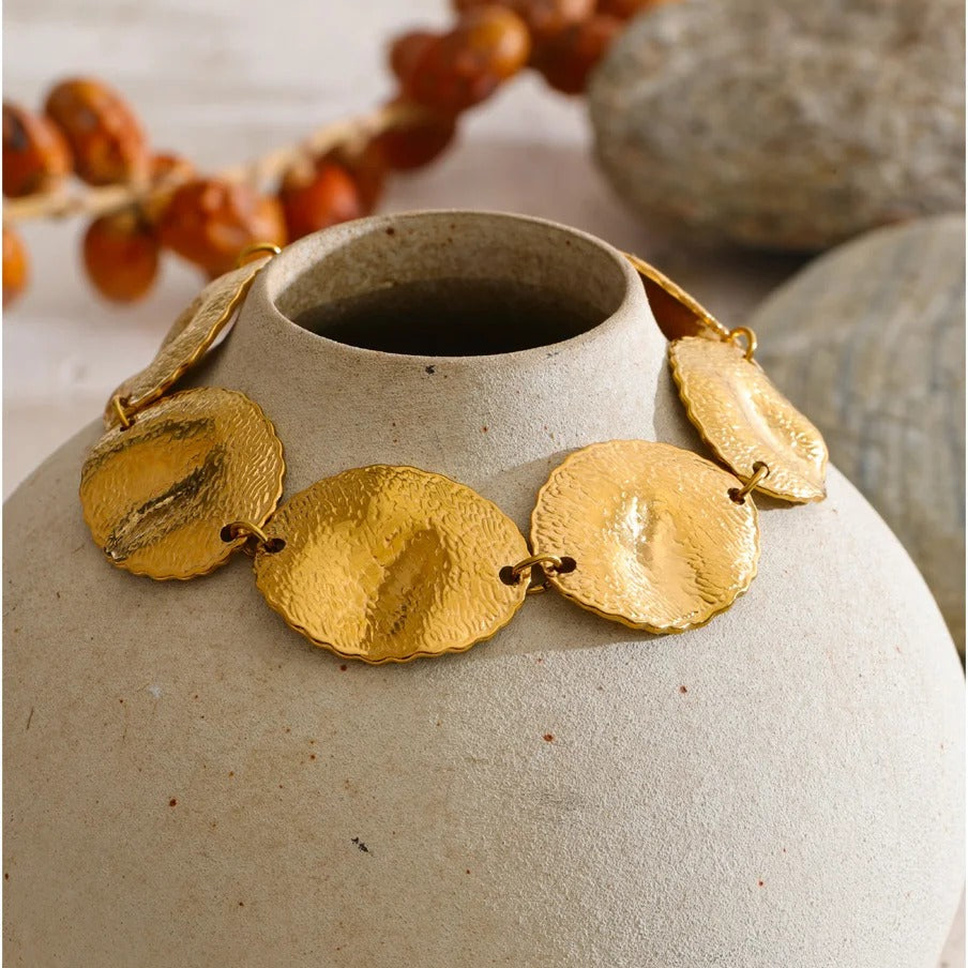 Blakely hammered gold-tone disc bracelet draped over a stone vase