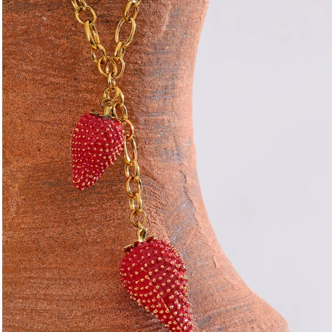 Jolie Strawberry Charm Necklace draped over a terracotta vessel