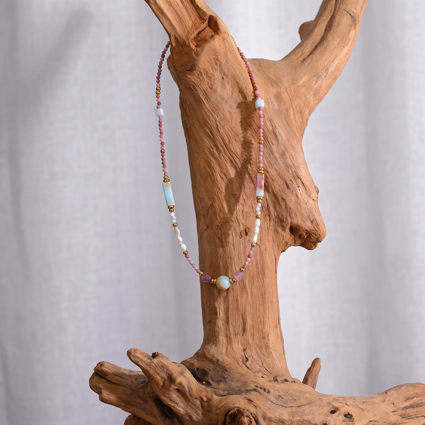Isla Pearl Bead Necklace draped over driftwood, angled view